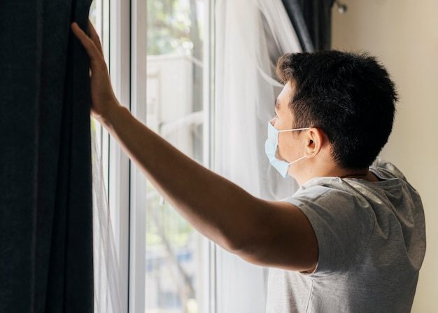 man-with-medical-mask-home-pandemic-opening-window-curtains_23-2148781392-6808710